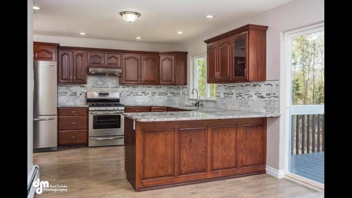 Kitchen remodel with stained wood cabinets, a stone-topped peninsula, tile backsplash, and stainless steel appliances